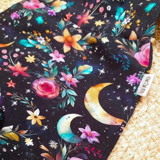 Close-up of Moon Garden print fabric featuring colourful flowers, crescent moons, and stars on a black background. Soft cotton for handmade kids clothing.