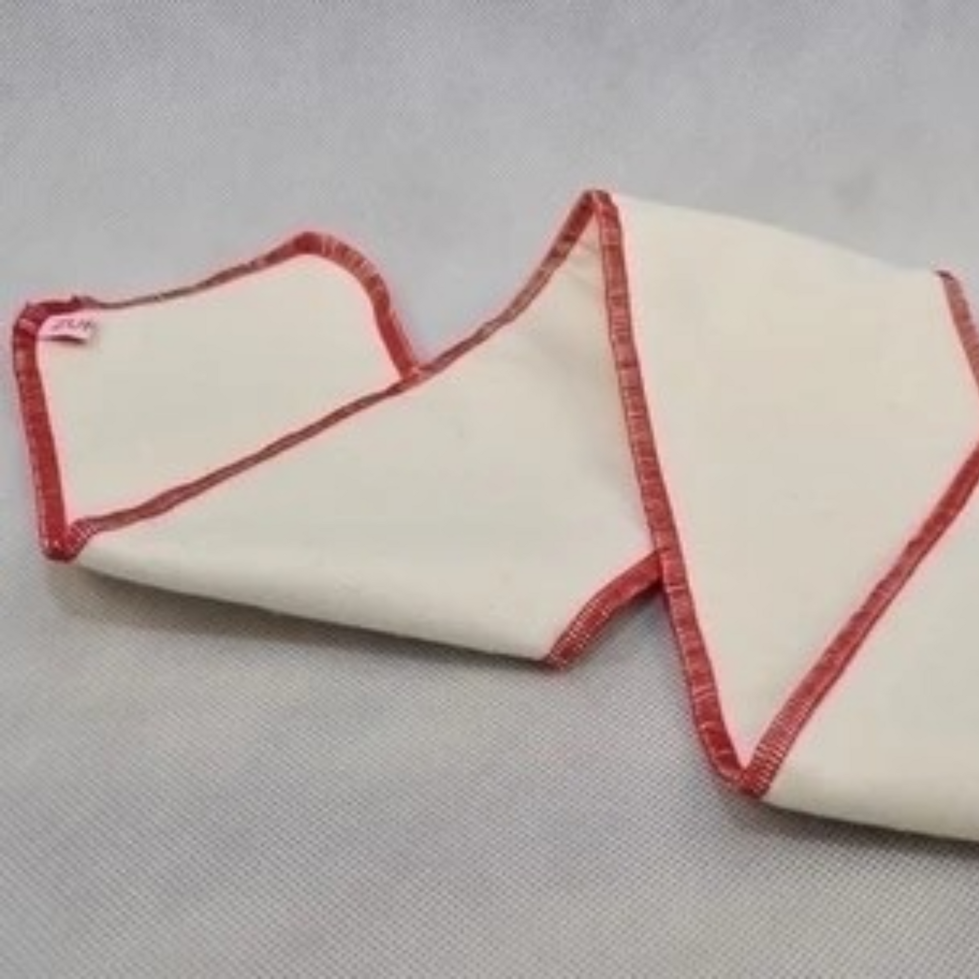 A very long, rectangular cotton cloth nappy insert with red stitched edges, folded in sections and laid on a grey textured background.